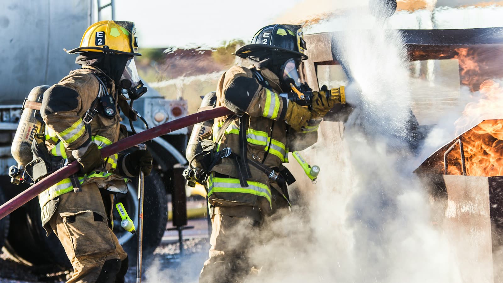 Firefighters spraying water on a fire, creating heavy smoke